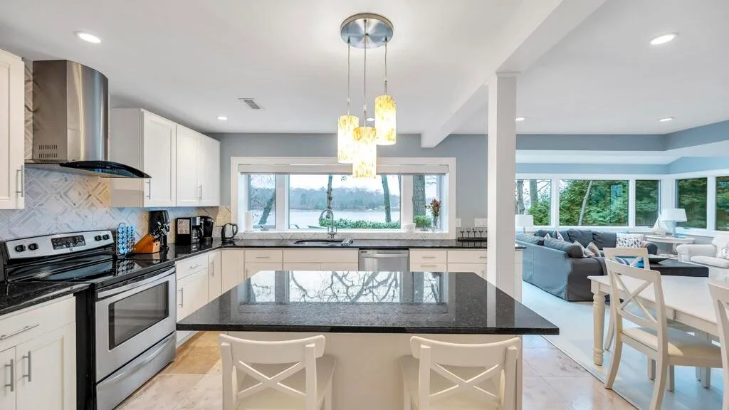 Una cocina luminosa de planta abierta, con una isla oscura y ventanas con vistas al agua.