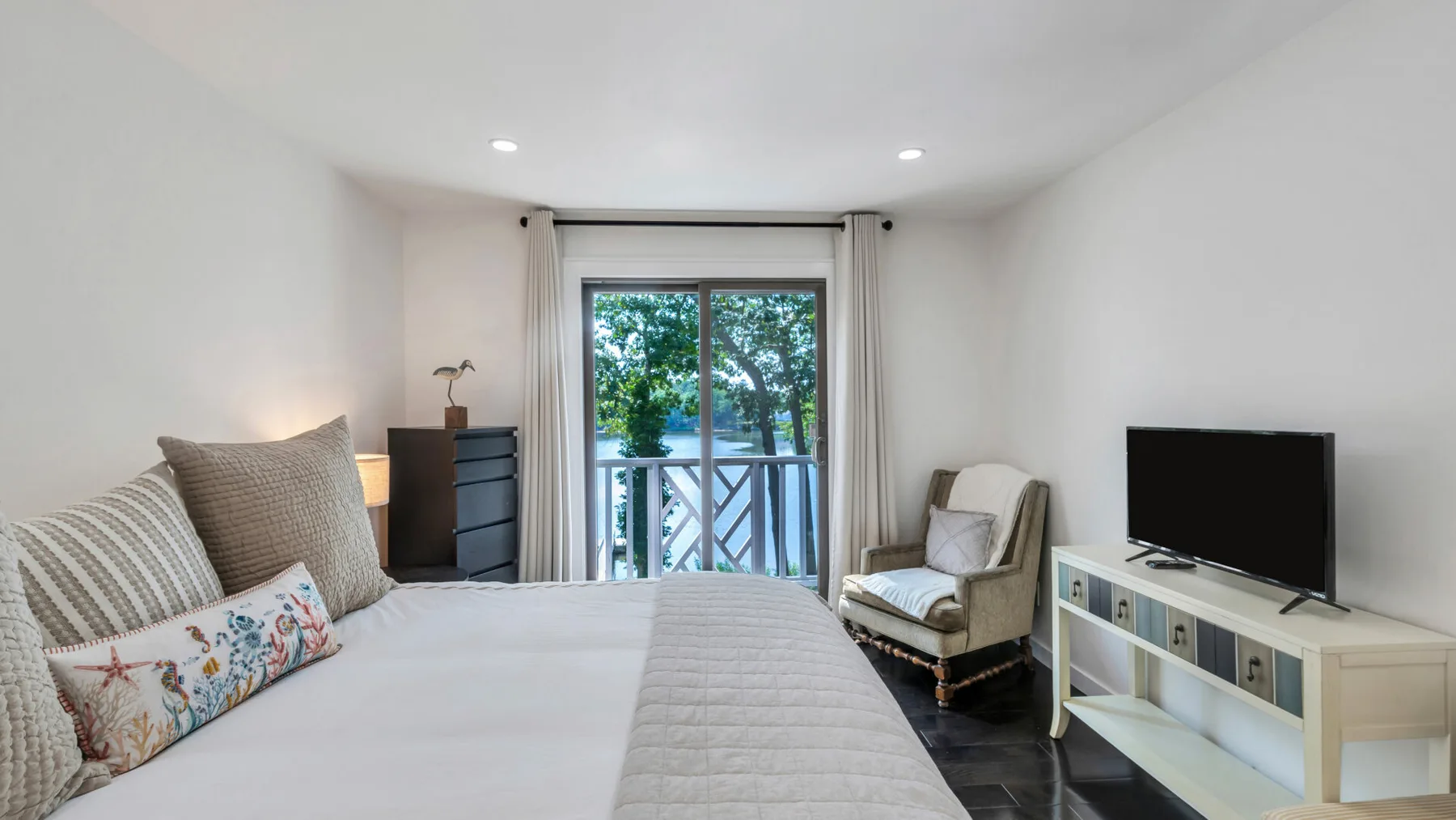 Un dormitorio luminoso con cama, asientos y un televisor junto a las puertas del balcón.