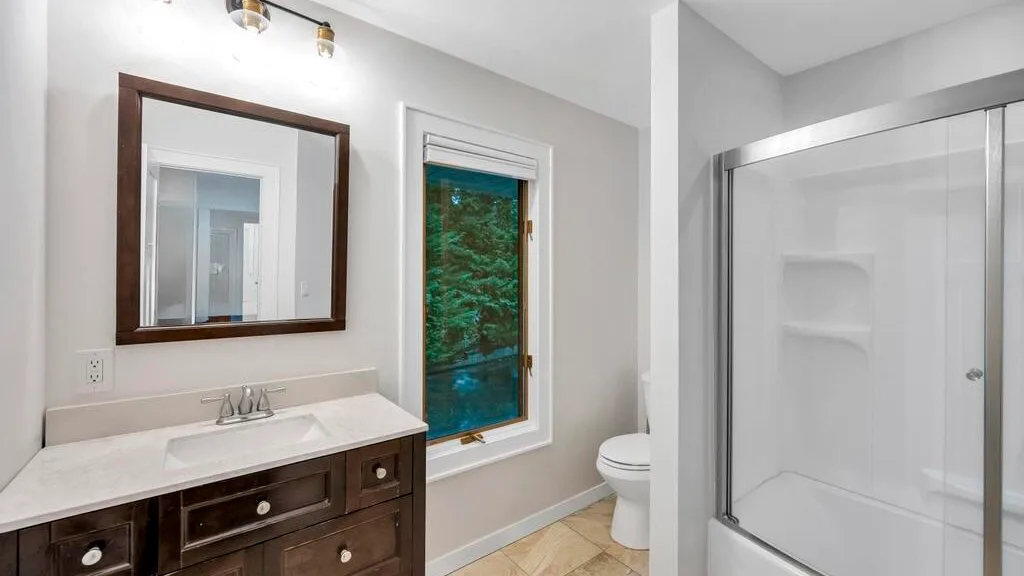 Un baño con lavabo, espejo, ventana, inodoro y ducha.