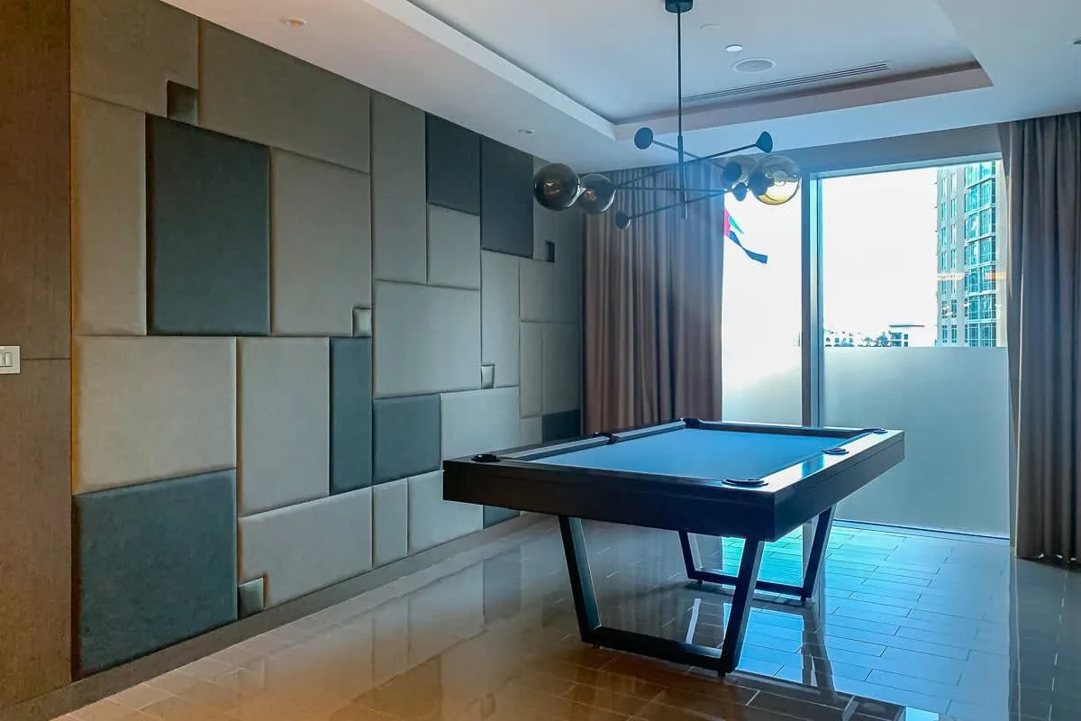 Una sala de juegos con una mesa de billar junto a grandes ventanas.