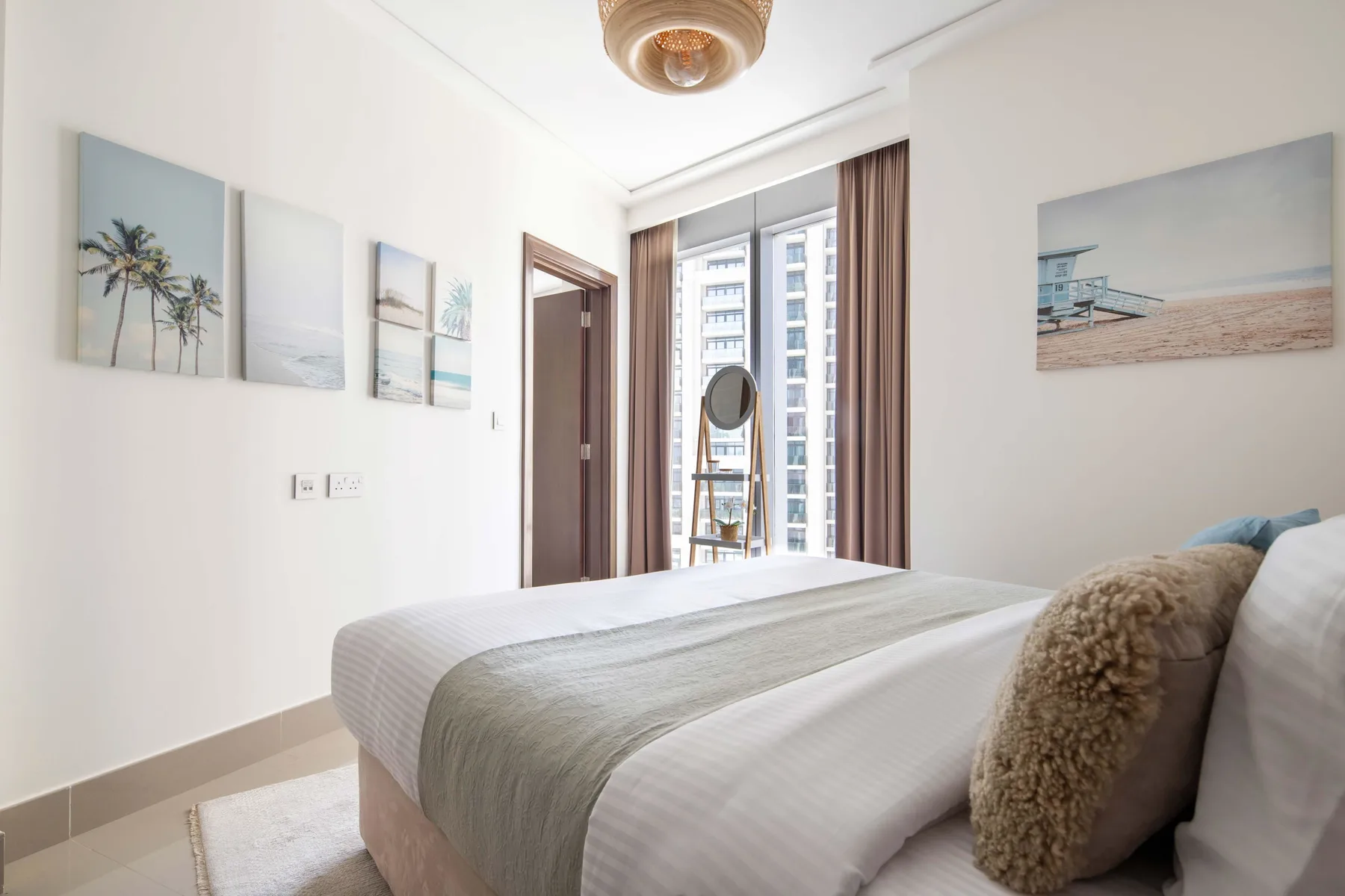 Un dormitorio luminoso con una cama tendida y láminas enmarcadas de la playa.