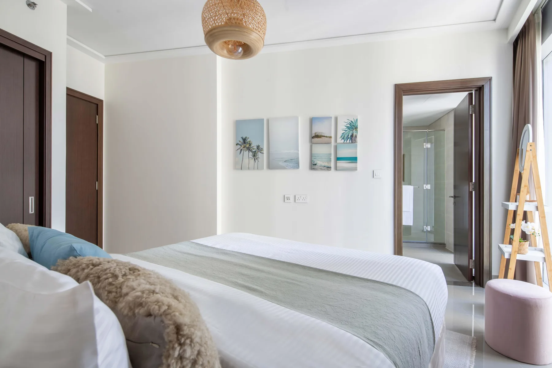 Un dormitorio luminoso con una cama tendida y láminas costeras enmarcadas.