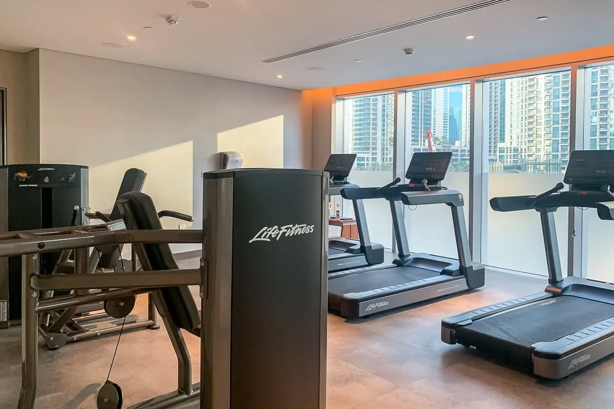 Una sala de ejercicio con cintas de correr y equipos de entrenamiento junto a grandes ventanas.