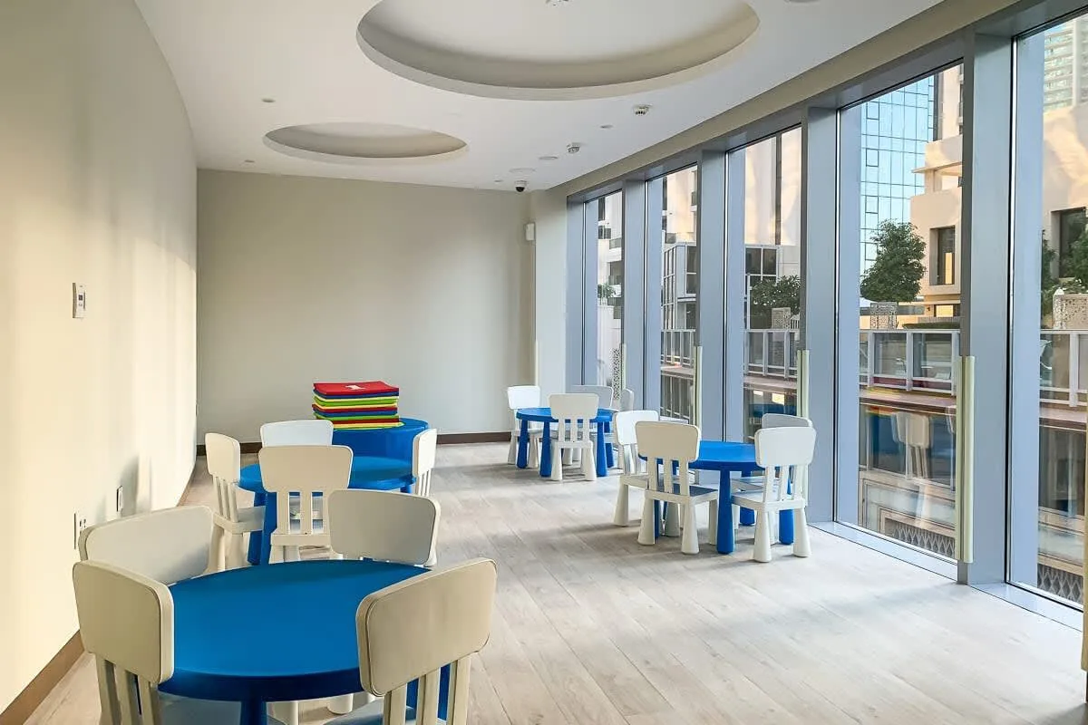 Un comedor interior luminoso con mesas azules y ventanas de suelo a techo.
