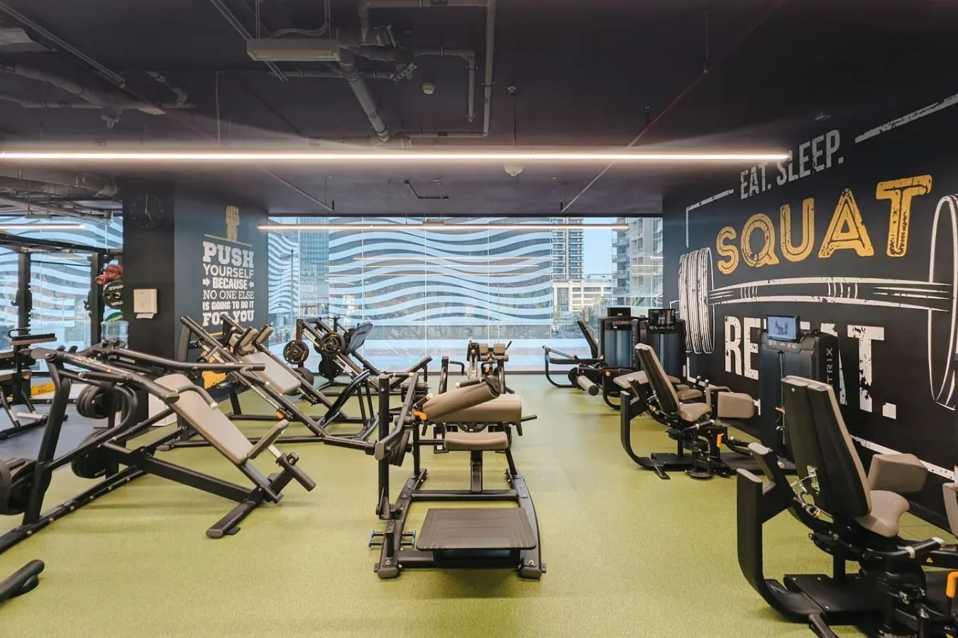 Un gimnasio con equipos de ejercicio y grandes ventanales.