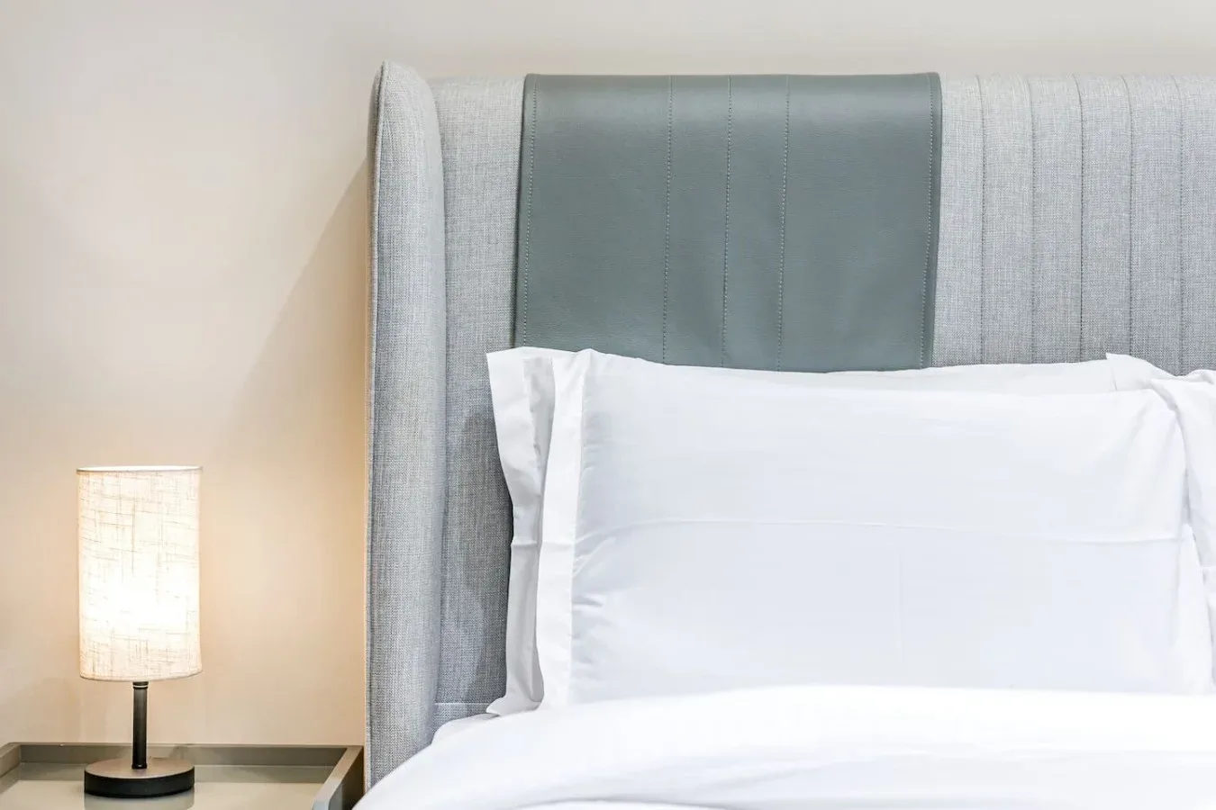 Una cama con ropa de cama blanca y un cabecero tapizado alto.