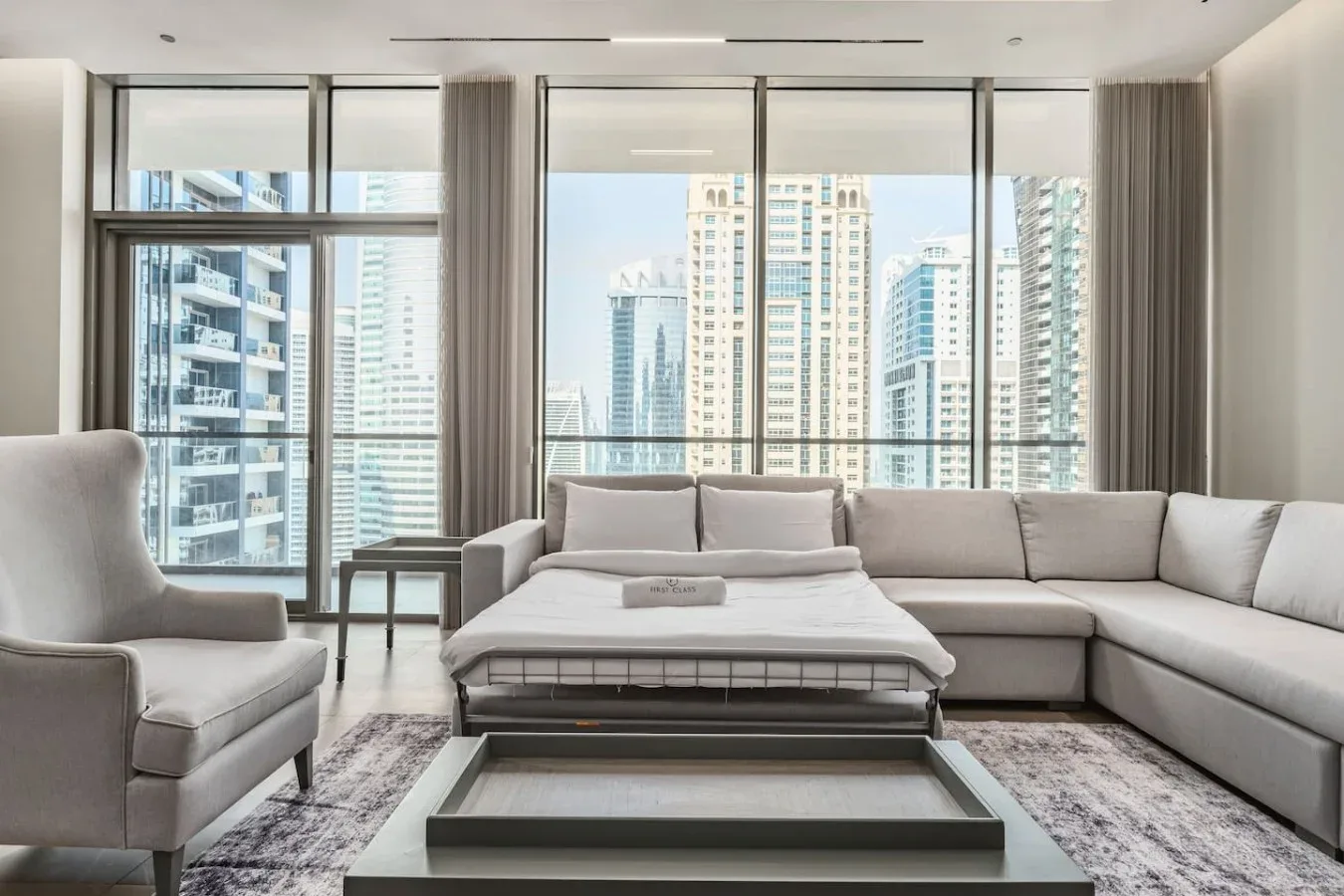 Una sala de estar moderna con asientos seccionales y amplias ventanas con vistas a edificios de la ciudad.
