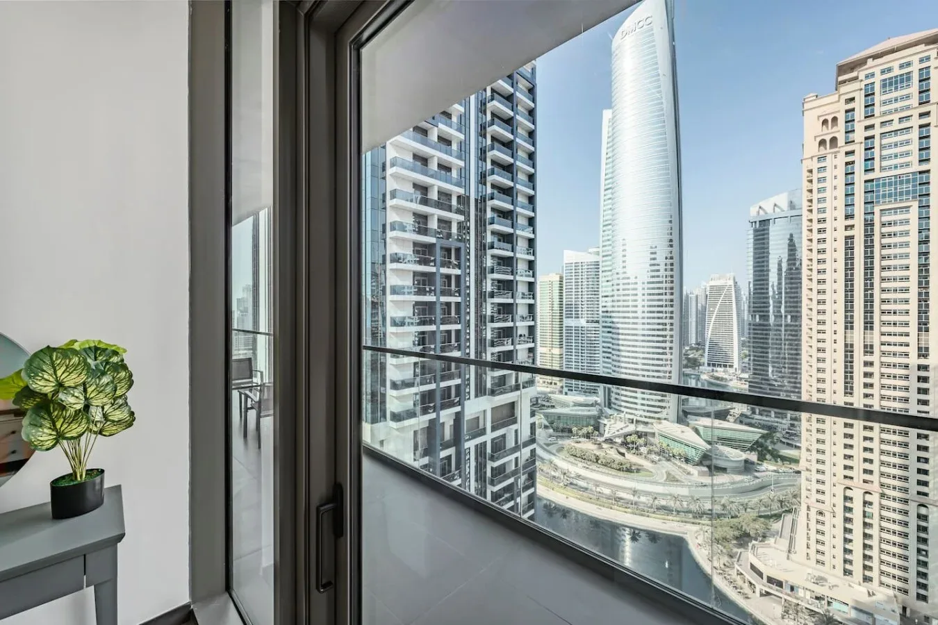 Se ve el perfil urbano a través de una gran ventana, con una planta en maceta cerca.