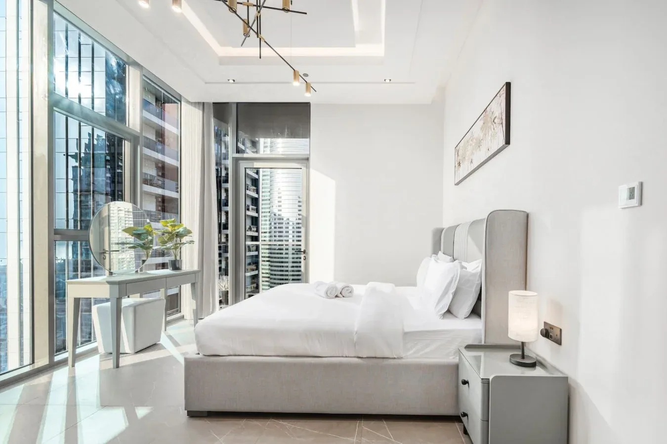 Un dormitorio luminoso con una cama bien arreglada junto a ventanales.
