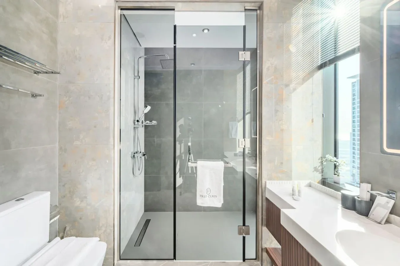 Un baño moderno con una ducha de vidrio y un tocador largo junto a la ventana.