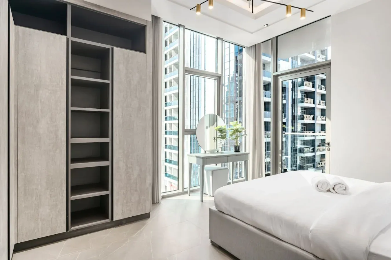 Un dormitorio con una cama, un tocador y ventanales de piso a techo.