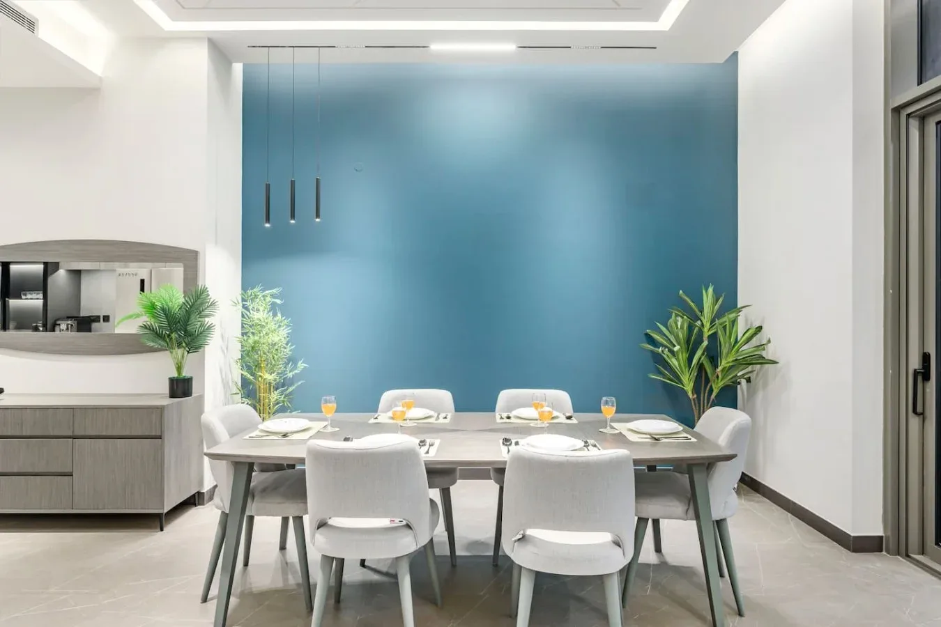 Comedor con mesa y asientos frente a una pared azul.