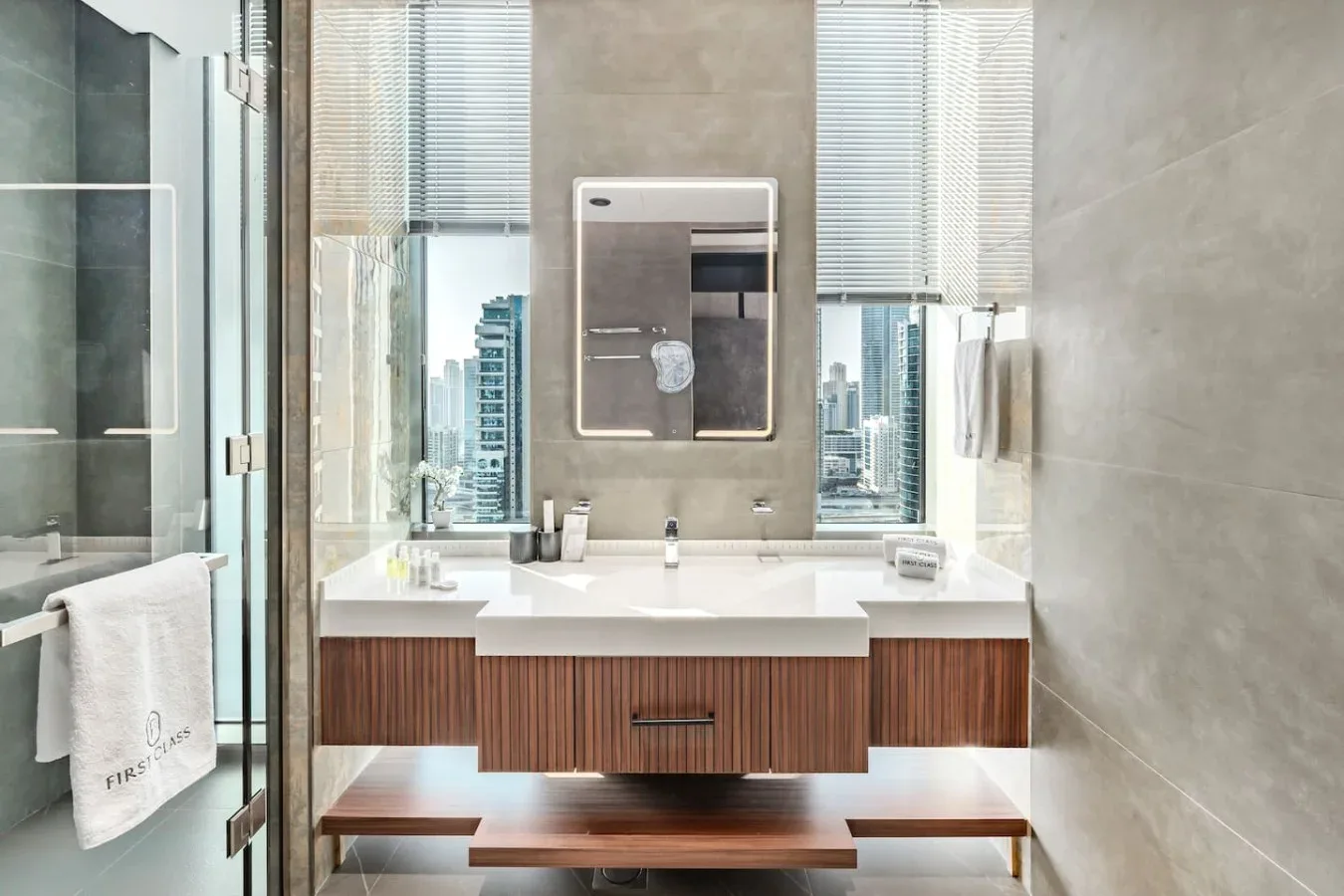 Un tocador de baño moderno está bajo ventanas altas con vistas a edificios de la ciudad.