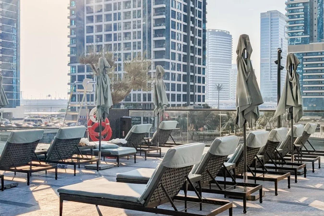 Una terraza exterior de piscina con tumbonas y sombrillas cerradas.