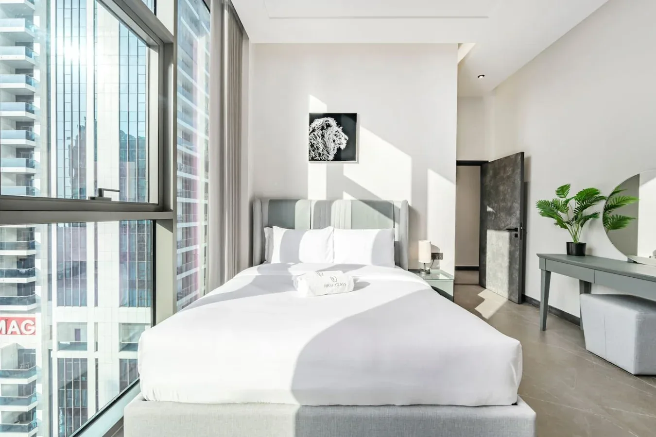 Un dormitorio luminoso con una cama bien tendida junto a ventanas de suelo a techo.