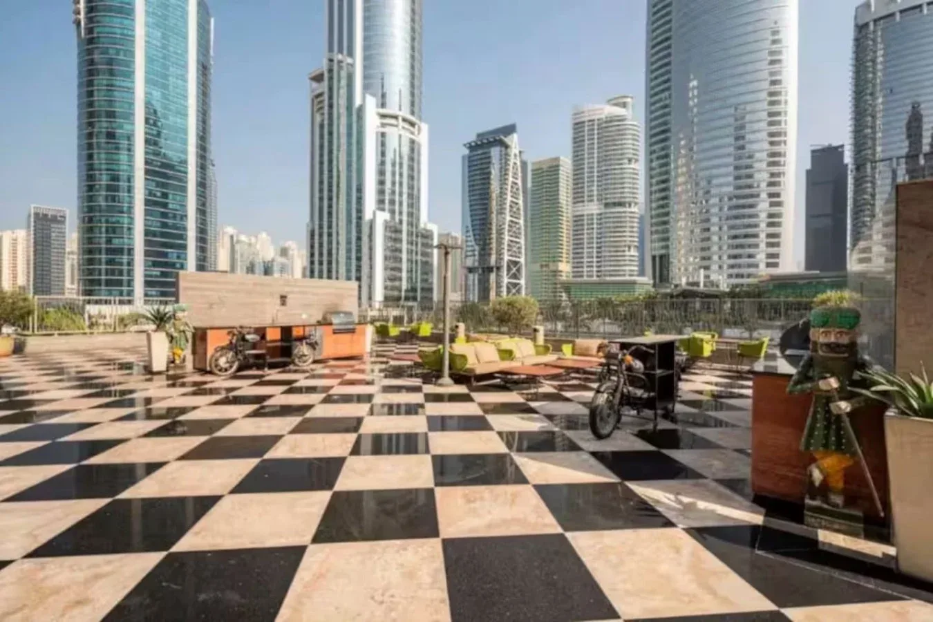 Una terraza con suelo a cuadros, asientos y edificios altos de la ciudad al fondo.