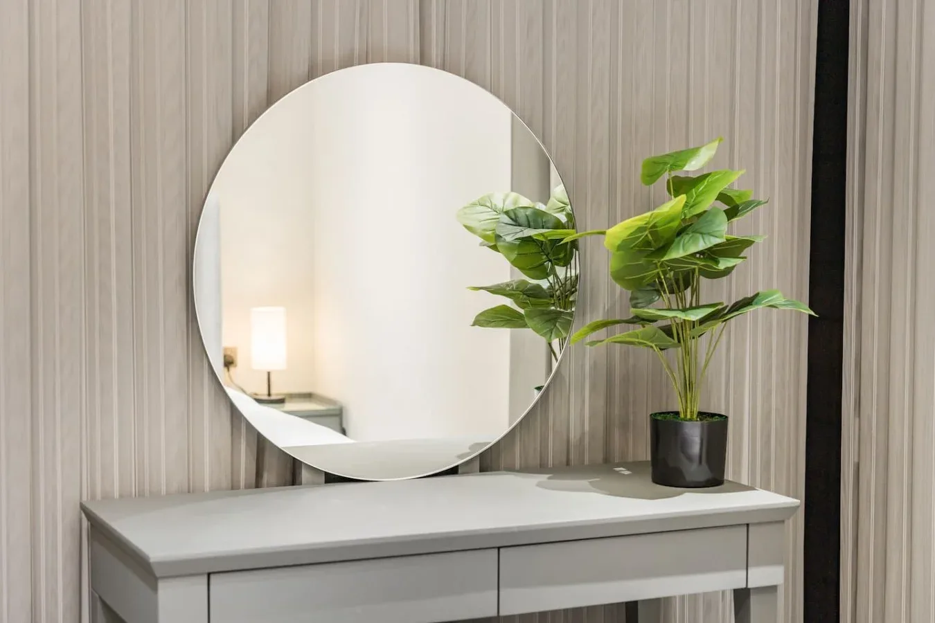 Un espejo redondo y una planta frondosa sobre una consola en una habitación.