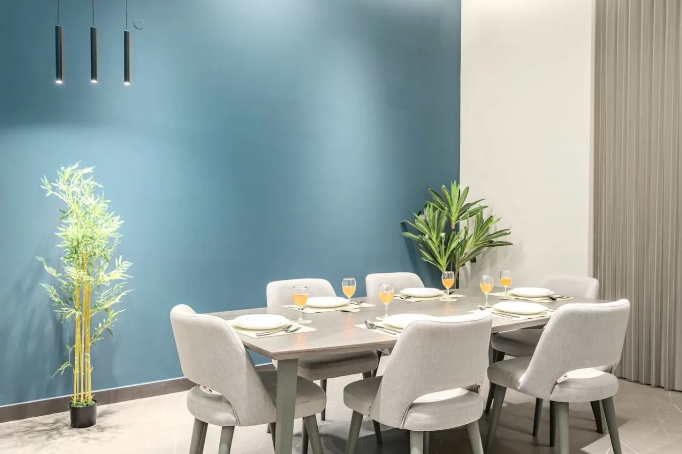 Comedor con una mesa, asientos tapizados y plantas en macetas.