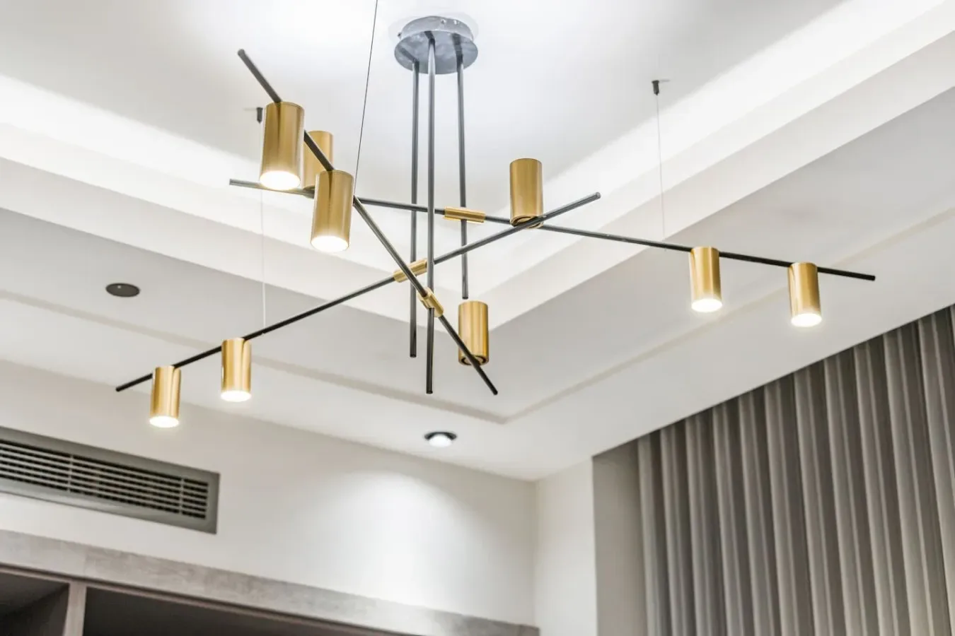 Una luminaria moderna cuelga del techo sobre una habitación con cortinas largas.