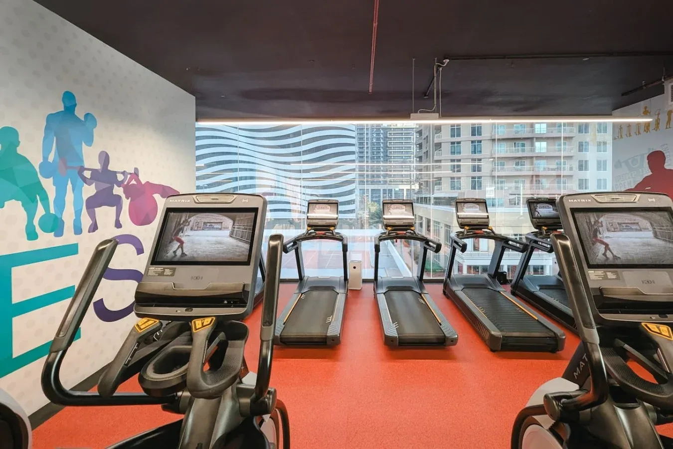 Un gimnasio con varias cintas de correr y siluetas coloridas de atletas en la pared.