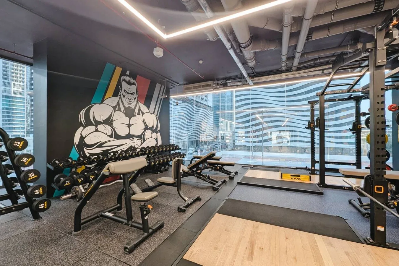 Un gimnasio con máquinas de pesas y un gran mural de una figura musculosa en la pared.