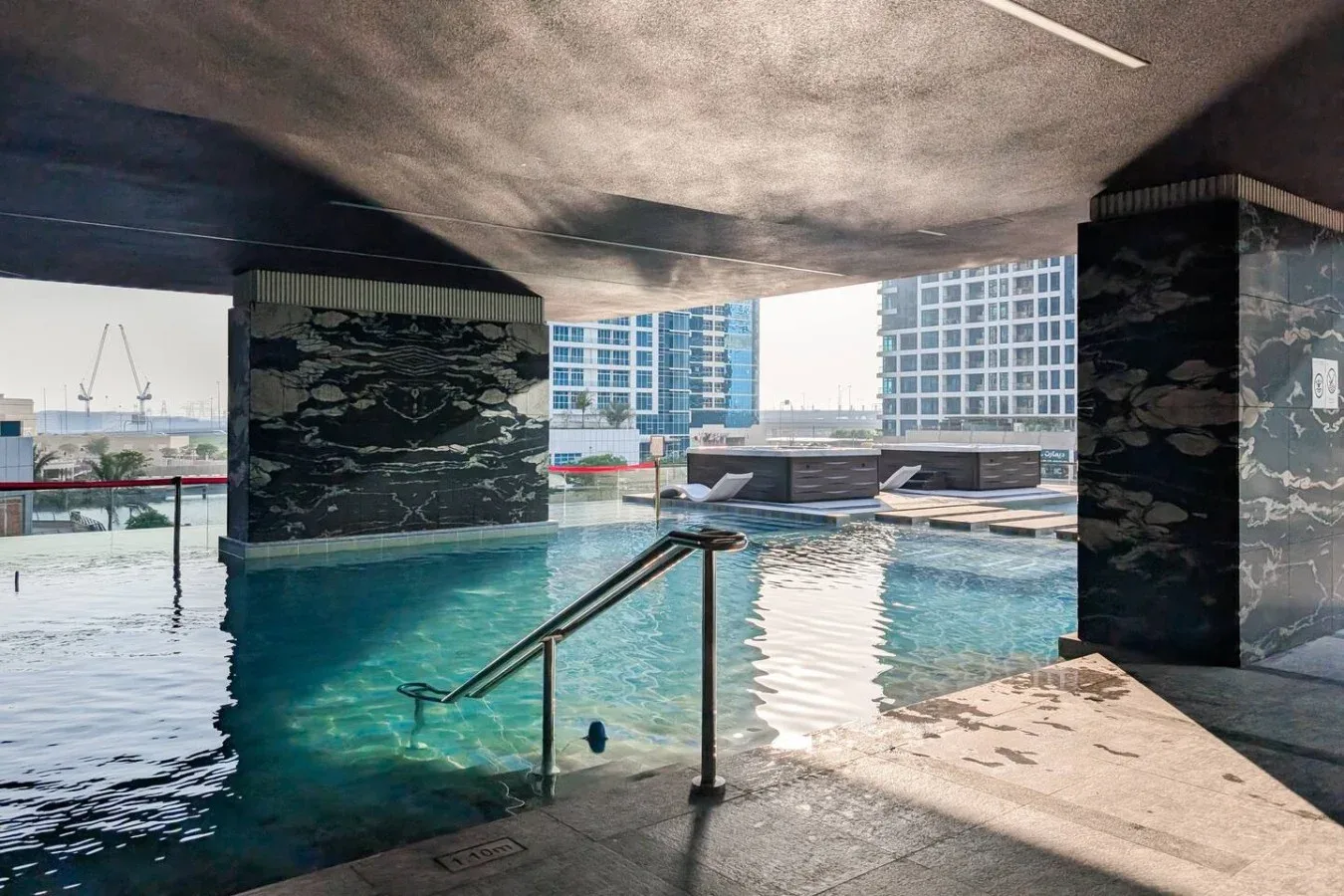 Una piscina en la azotea bajo un techo sombreado, con edificios de la ciudad al fondo.
