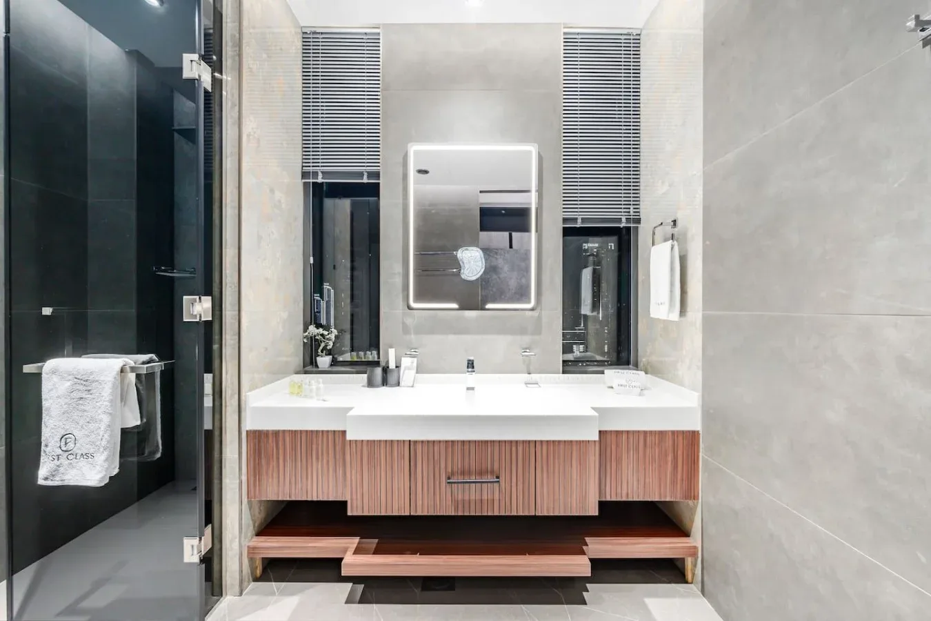 Un tocador de baño moderno con un espejo amplio y una ducha de vidrio oscuro.