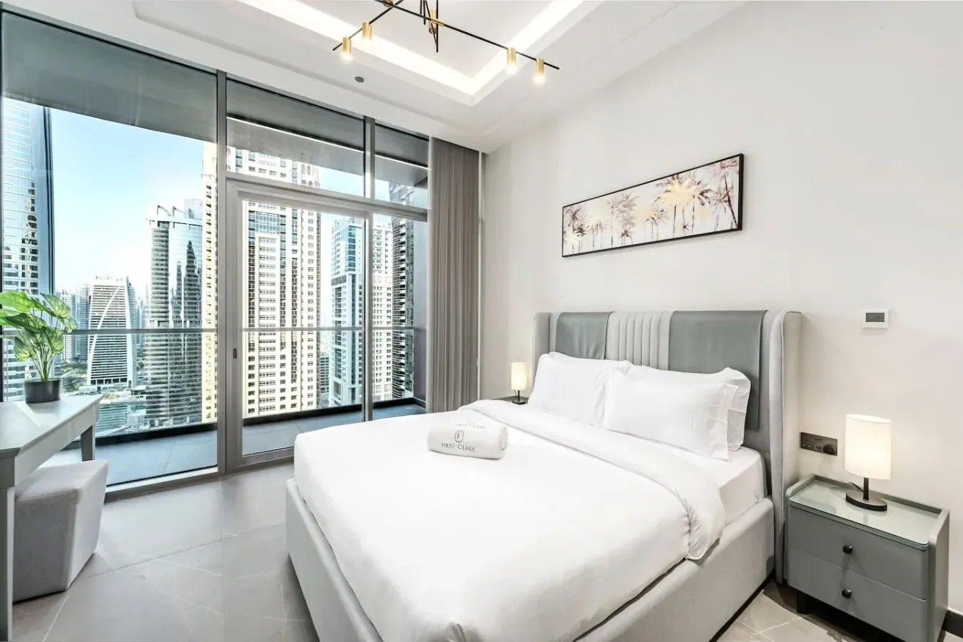 Un dormitorio luminoso con una cama tendida junto a ventanales de piso a techo.