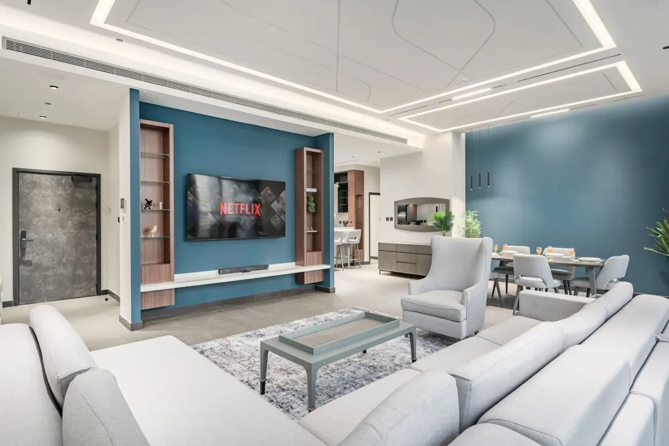 Una sala de estar moderna con asientos claros frente a un televisor en una pared azul.