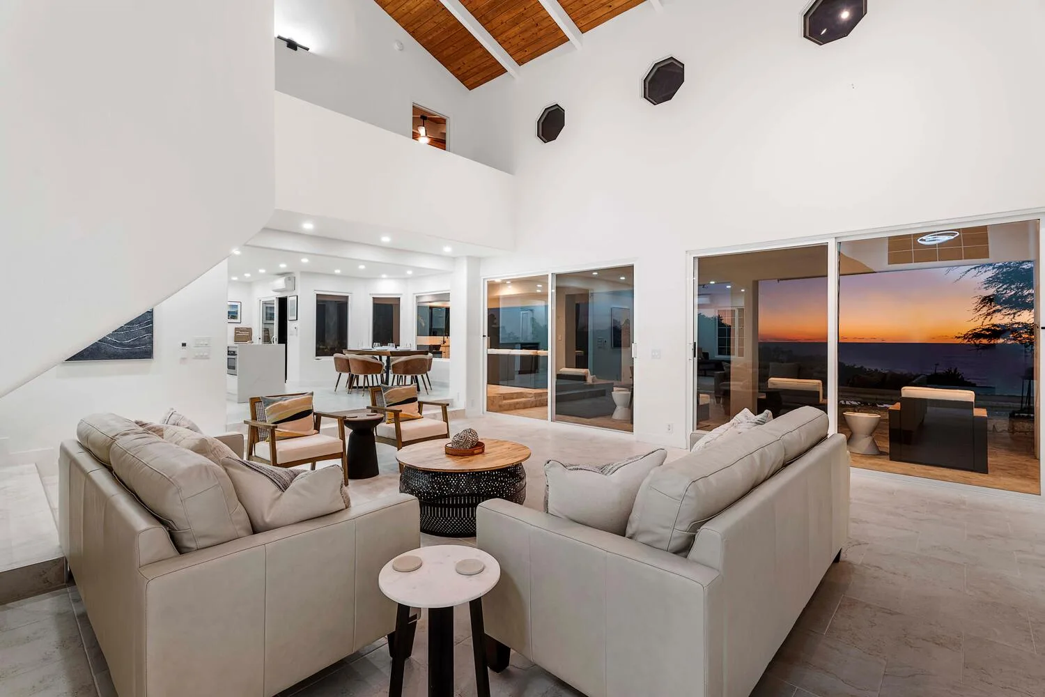 A bright living room with seating and large glass doors opening onto a sunset view.