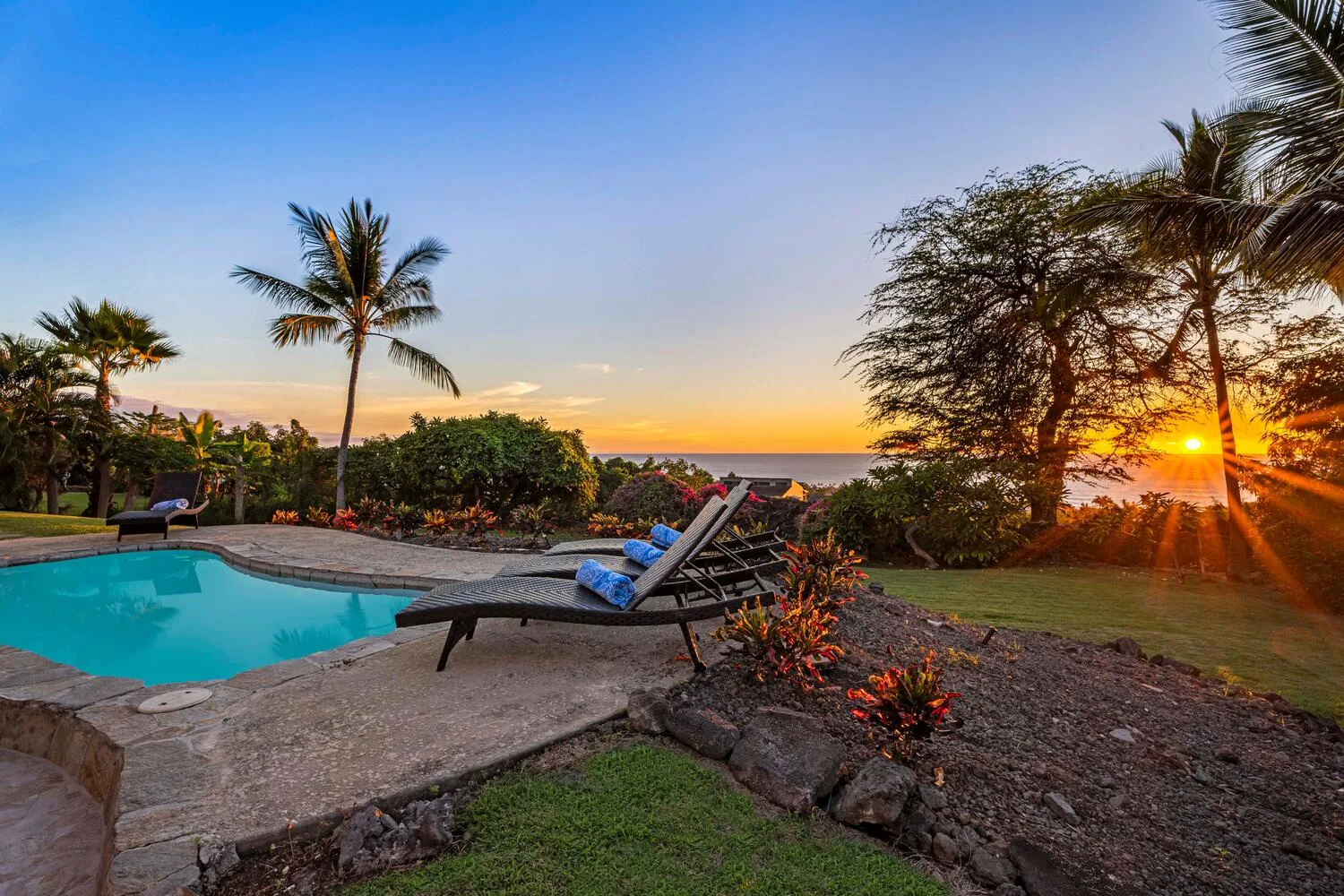 A swimming pool and lounge seating overlook the ocean at sunset.