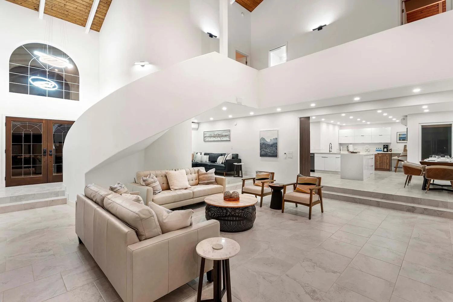 A spacious living room with light seating beneath a sweeping curved staircase.