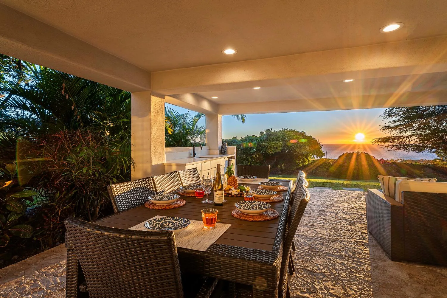 A covered outdoor dining area opens onto a garden and a sunset view.