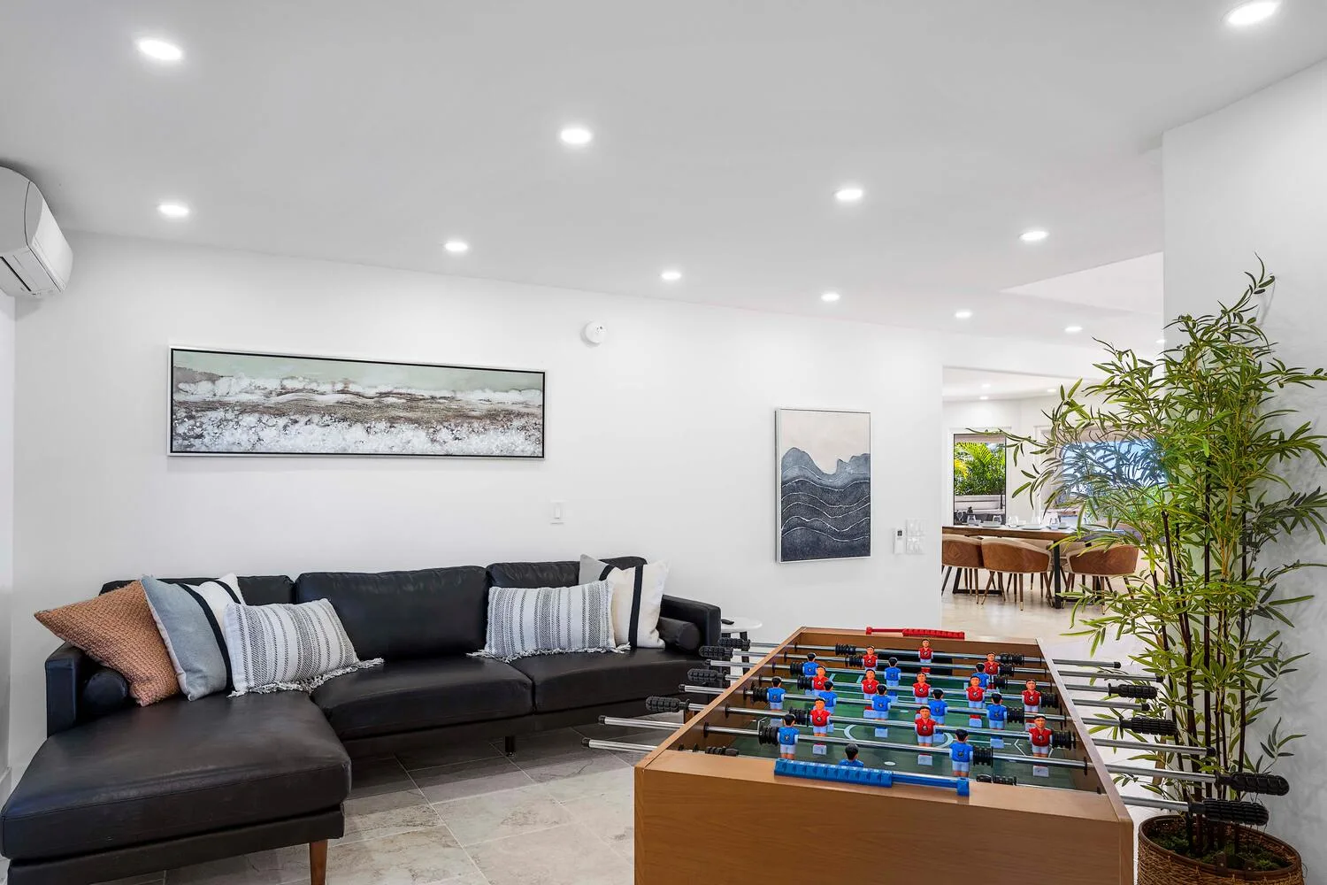 A bright living room with a dark sectional and a foosball table.
