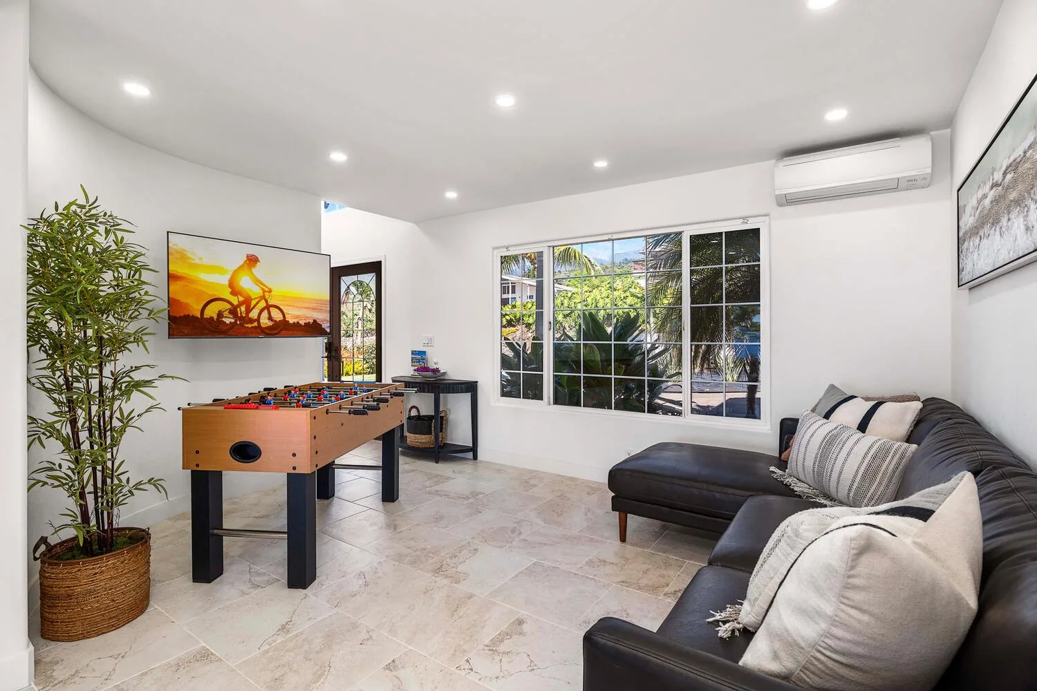 A bright living room with a sectional sofa, foosball table, and large windows.
