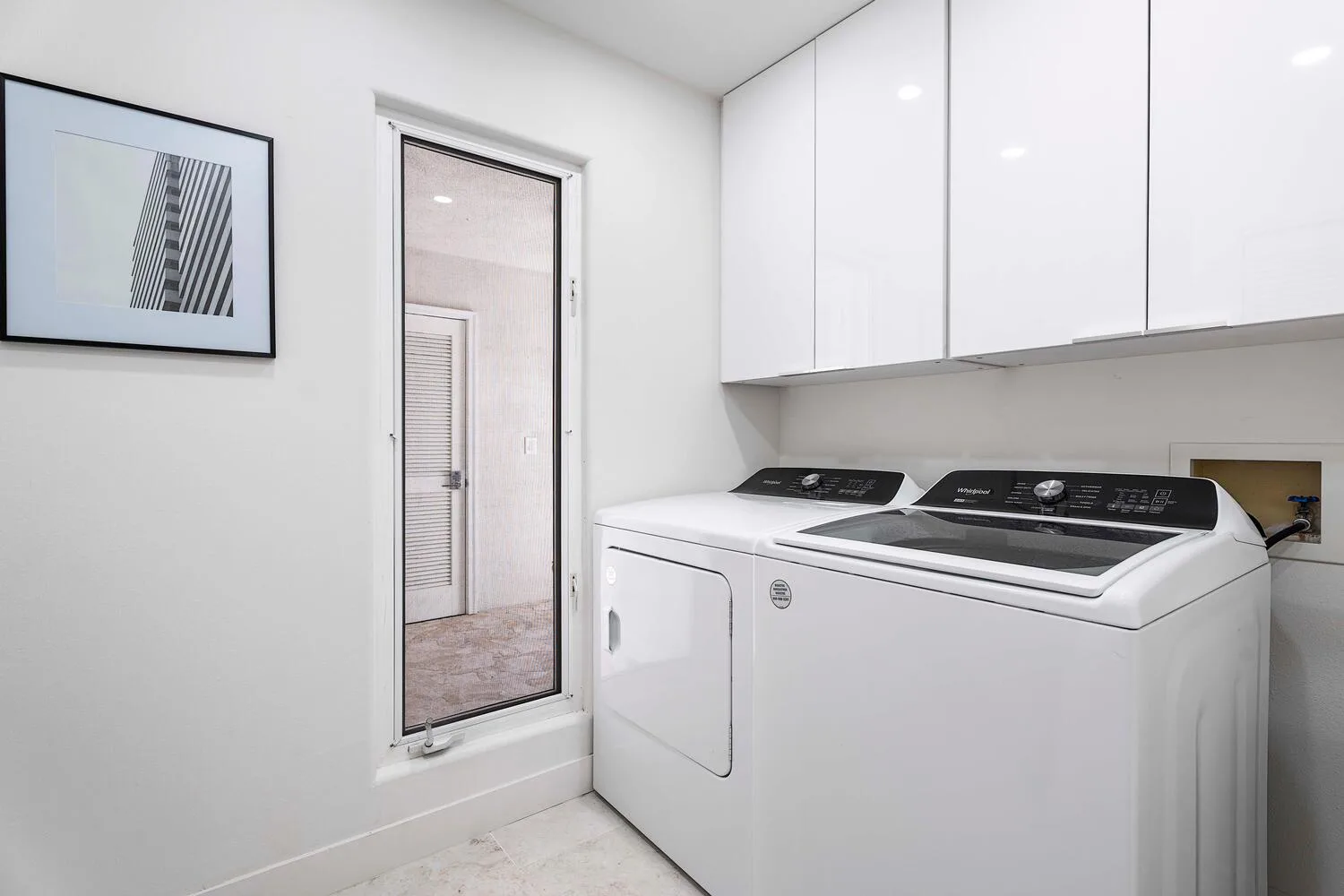 A laundry area with a washer and dryer beneath white cabinets.