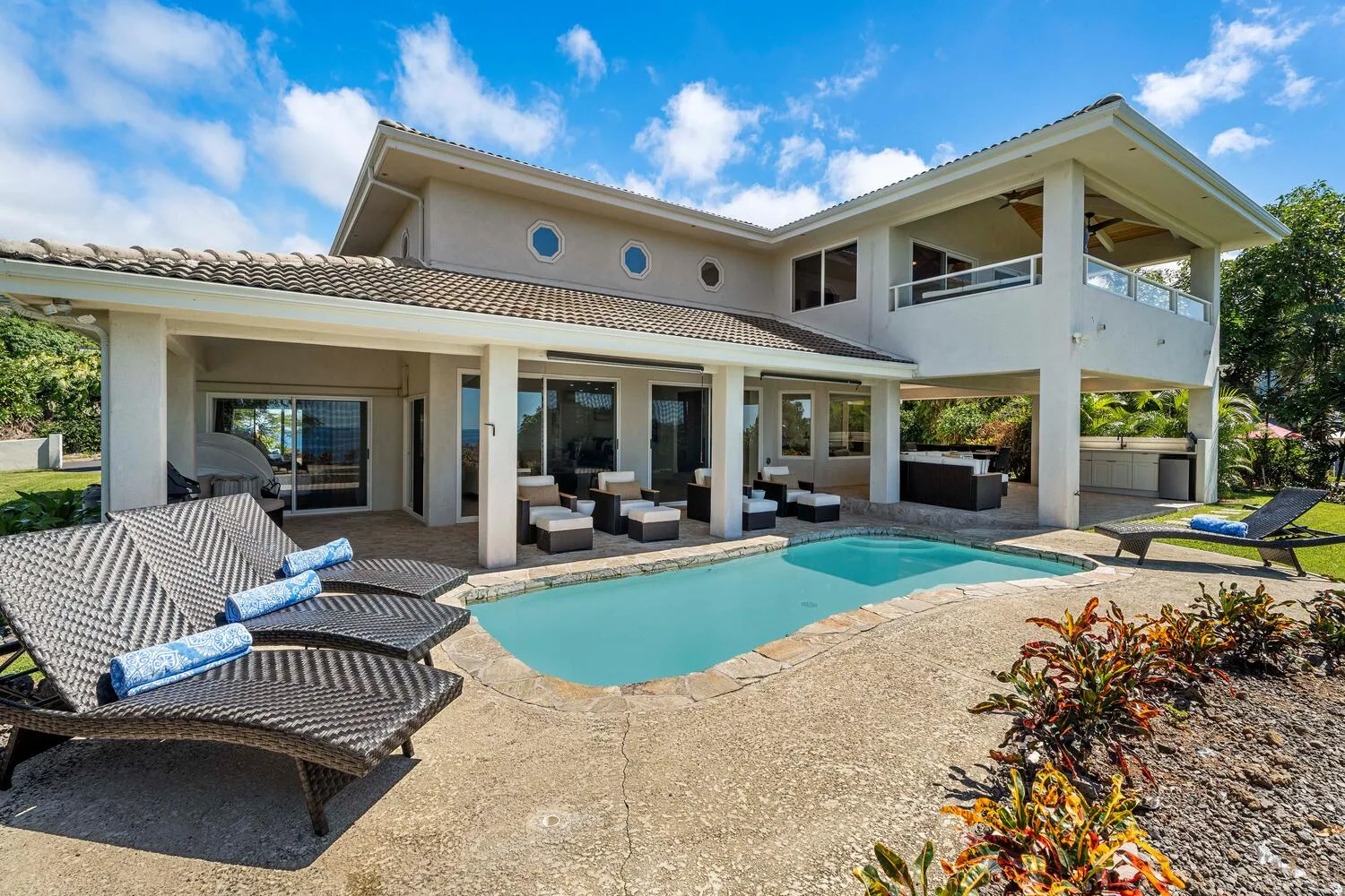 A modern house opens onto a swimming pool, patio seating, and landscaped gardens.