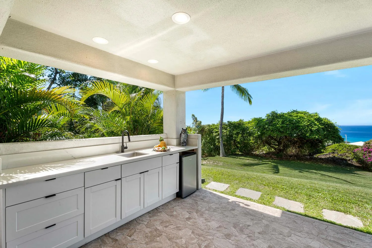 A covered outdoor kitchen opens onto a garden with a view of the ocean.