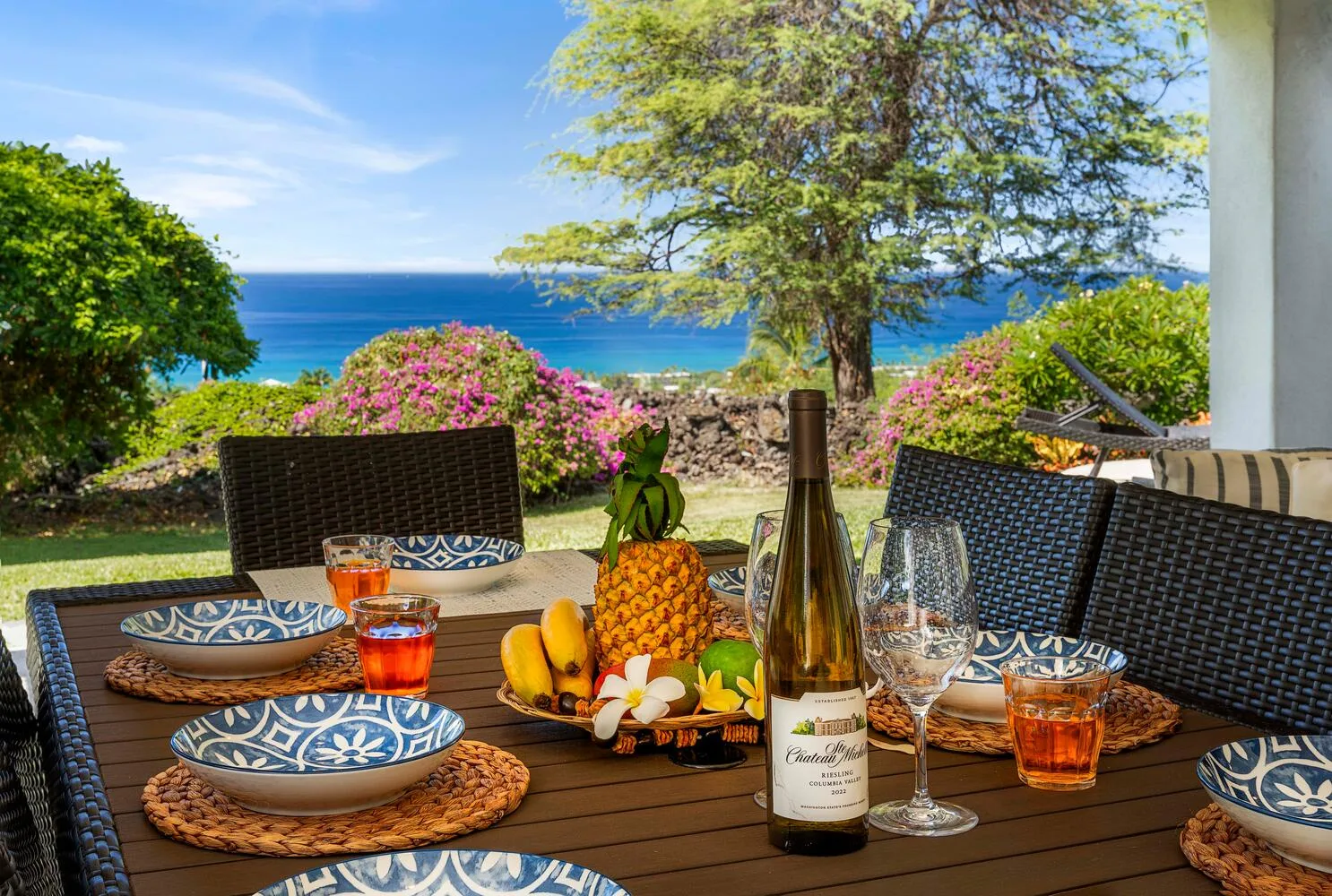 A dining table set with fruit and drinks overlooks a garden and the sea.