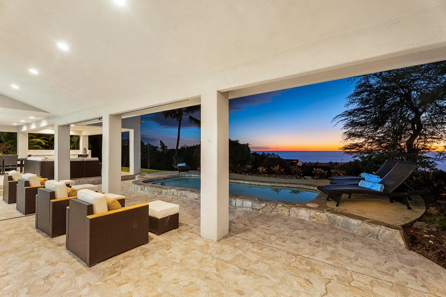 A covered patio with outdoor seating overlooks a pool and the sunset.