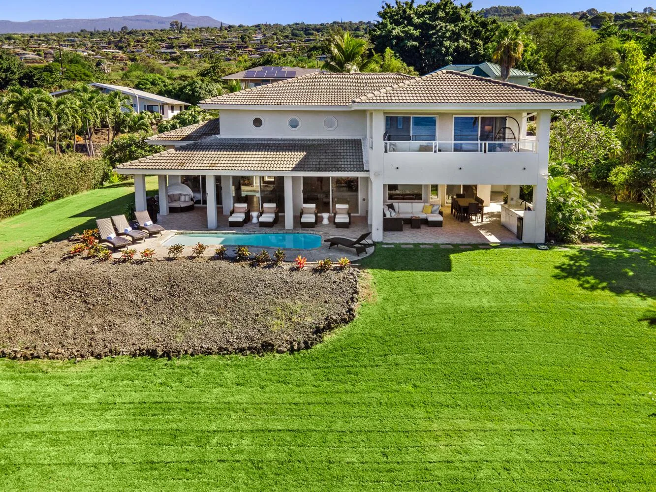 A large house overlooks a lawn, patio, and swimming pool.