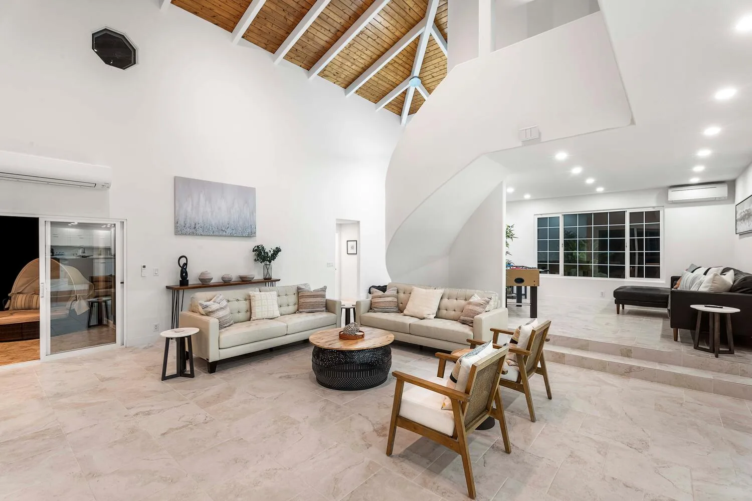 A spacious living room with light seating and a high, exposed-beam ceiling.