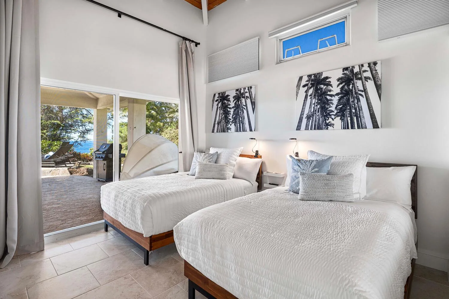 A bright bedroom with two beds and sliding glass doors opening onto a patio.