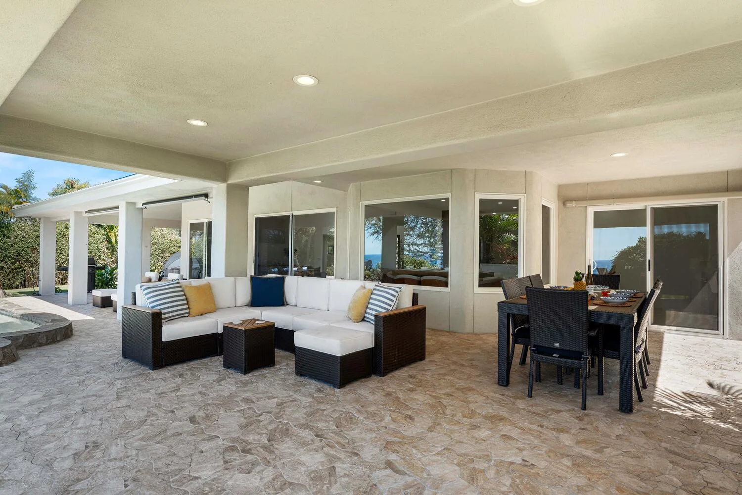 A covered outdoor patio has lounge seating beside a dining table.