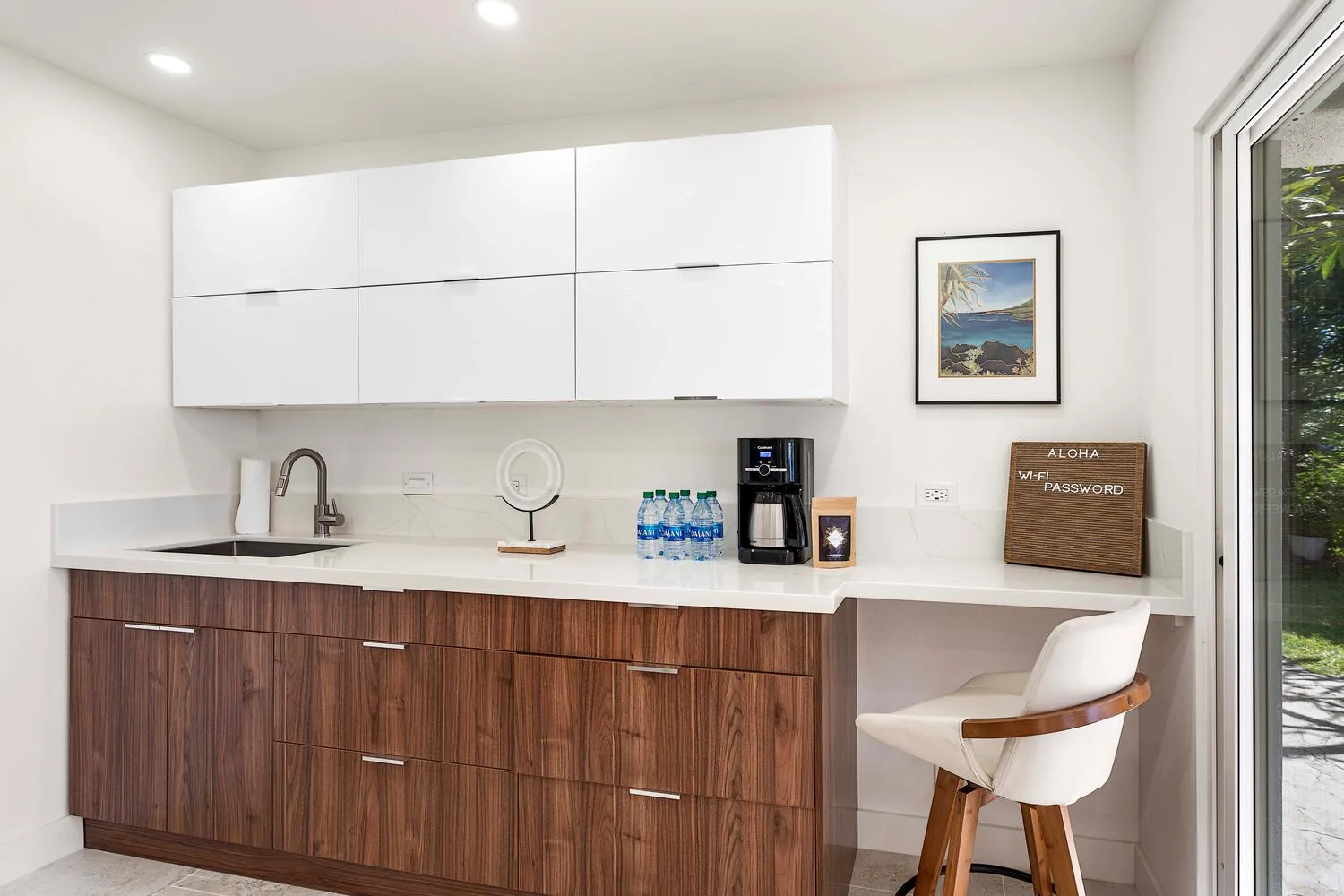 A bright kitchenette with white cabinets, a wood-toned counter, and a bar seat.