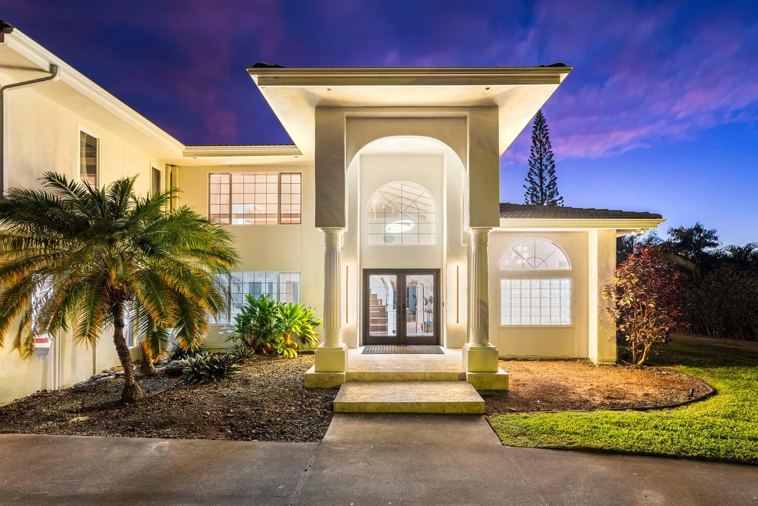 A large house entrance with arched windows and a landscaped front yard.