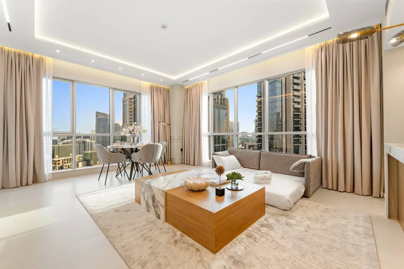 Una sala luminosa con zona de estar, comedor y grandes ventanales con vistas a edificios cercanos.