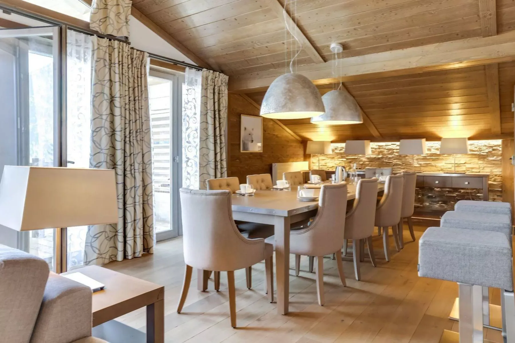 A dining area with a long table, upholstered seating, and pendant lights.