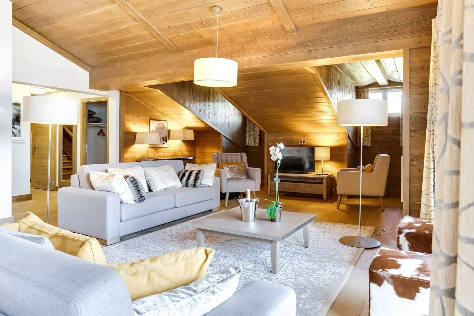 A living room with seating, a coffee table, and a television beneath a sloped wooden ceiling.