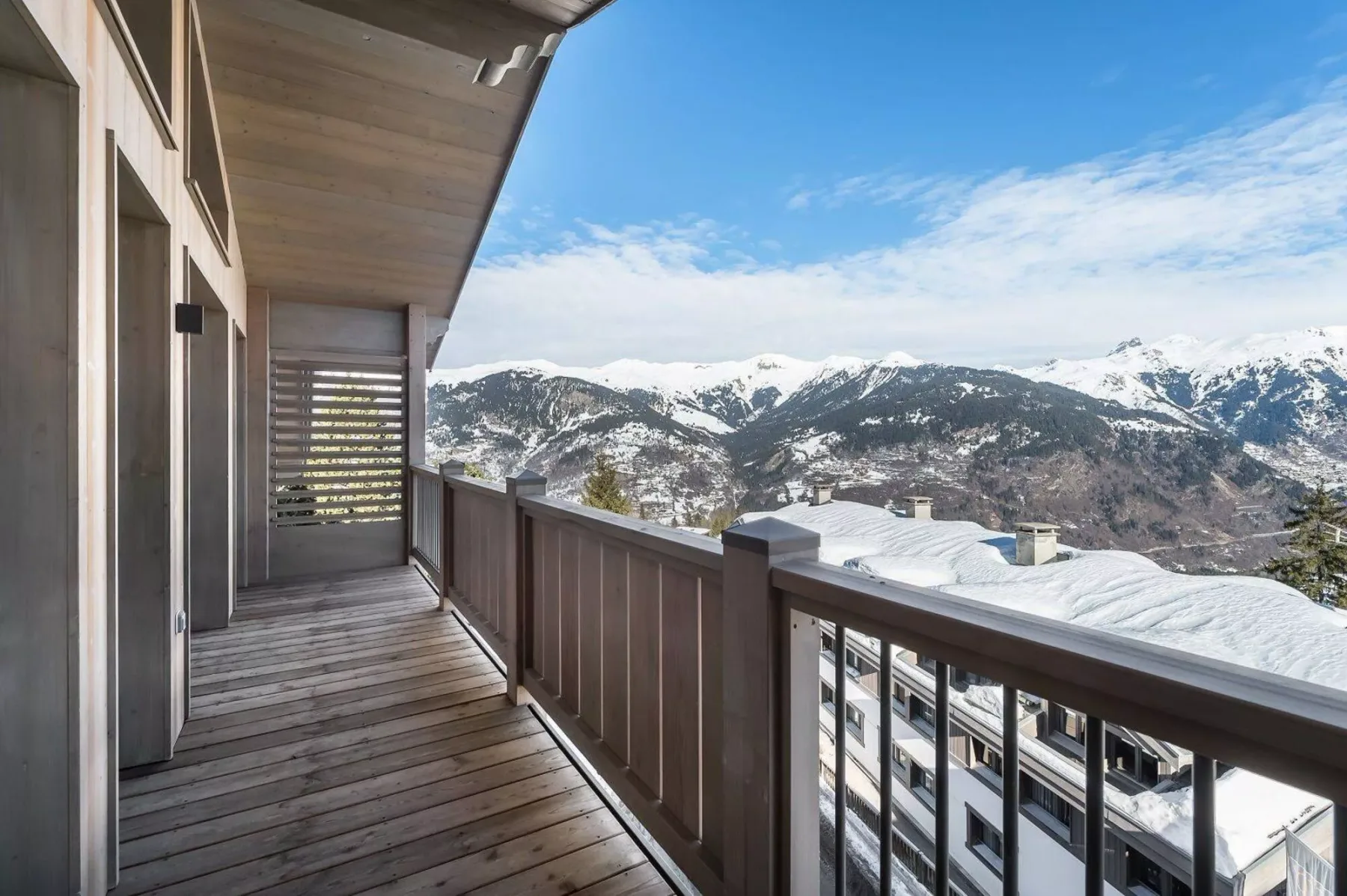 A wooden balcony overlooks snow-covered mountain peaks and buildings.